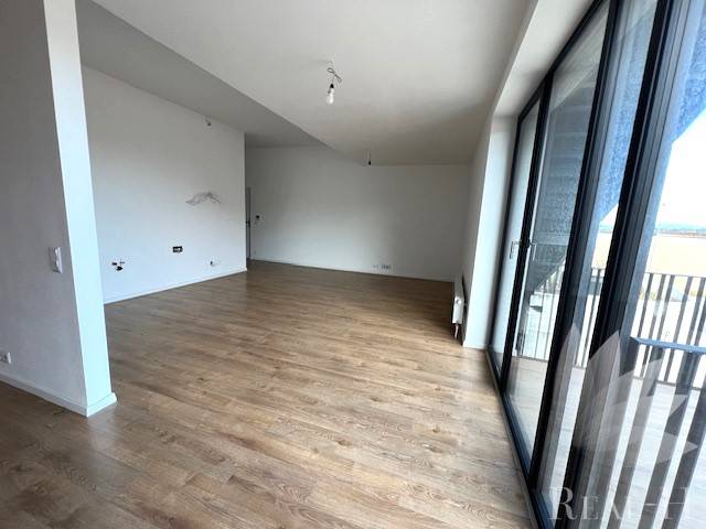 Spacious living room with wood-patterned flooring in a 2-room apartment with glass doors to the balcony.