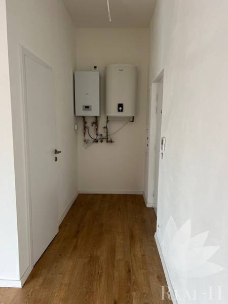 A hallway in a 2-room apartment with a wood-patterned floor and a boiler on the wall.