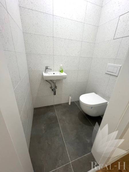 A small bathroom in a 2-room apartment with a toilet, sink, and gray tiles.
