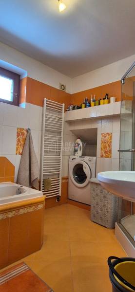A bathroom in a family house with a washing machine, shower, bathtub, and colorful tiles.