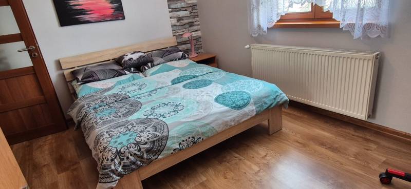 A bedroom in a family house with a bed, a radiator, and a floor with a wooden decor.
