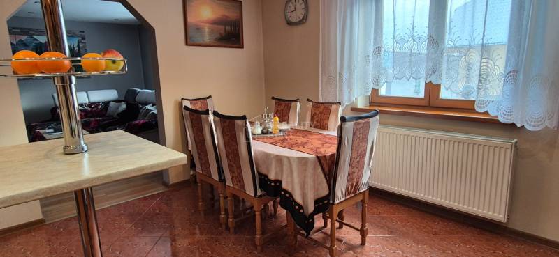 Dining table with six chairs, curtains, and decorative fruit in a family house.