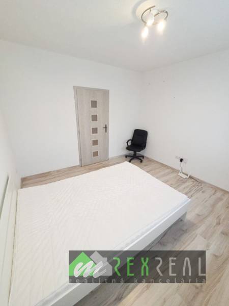 Bright bedroom in a 3-room apartment with wood-patterned flooring and an office chair.