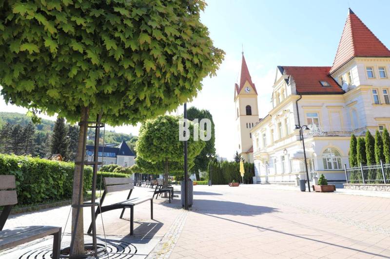 A sidewalk with benches and a historical building in Trenčianske Teplice, plots - housing.