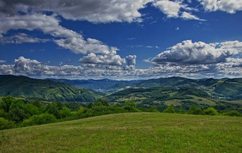 Hills and meadows around Žarnovica under the blue sky, agricultural and forest lands.