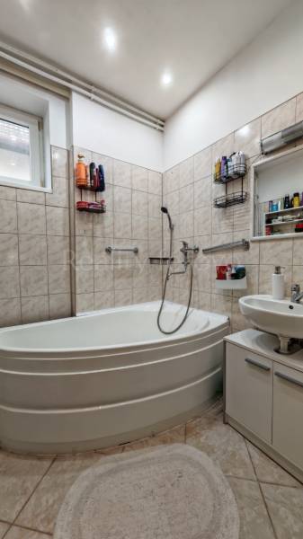 A bathroom in a family house with a corner bathtub, a sink, and white tiles.