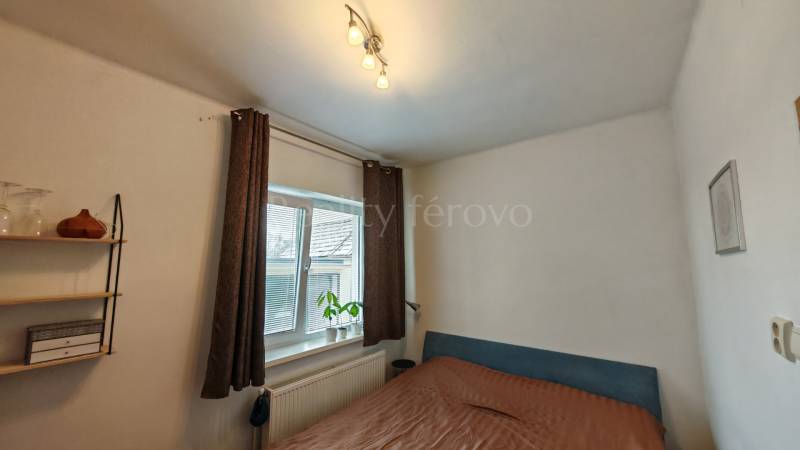 Bedroom in a family house, with a bed, shelves, and a window with a decorative plant.