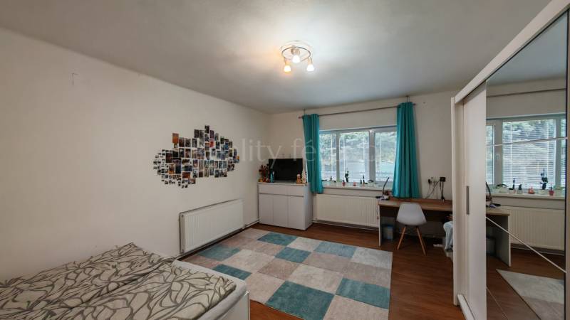 A room in a family house with a desk, a bed, photos on the wall, and a floor with a wooden decor.