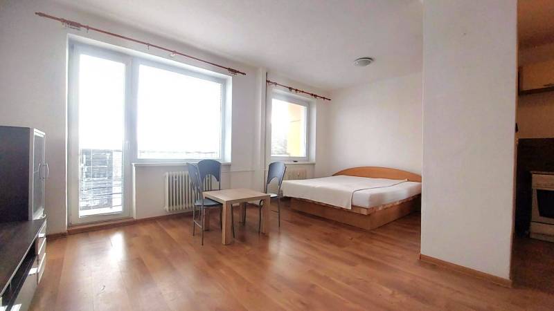 A studio apartment with a bed, table, chairs, and a wooden decor floor.