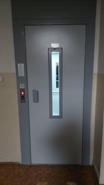 Gray elevator doors in the interior of a one-room apartment with a control panel on the side.