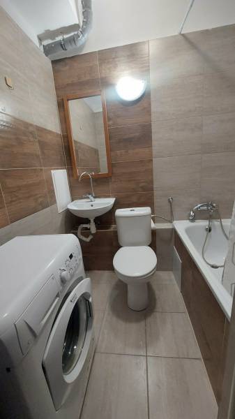 Bathroom in a studio apartment with a bathtub, sink, and washing machine, tiled with ceramic tiles.