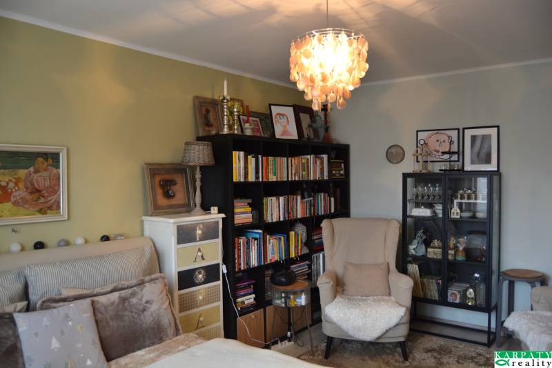 A room in a three-room apartment with an armchair, a bookshelf, chandeliers, and wall decorations.