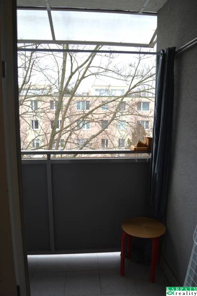 A balcony of a 3-room apartment with a view of the surrounding architecture and a tree in the background.