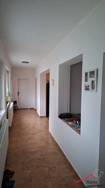 A hallway of a family house with tiles and white walls, with an open door on the right side.