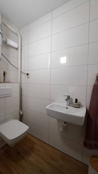 Bathroom in a 2-room apartment with white tiles and a wooden decor floor.