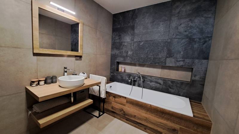 A bathroom in a 2-room apartment with a bathtub, a mirror, and a sink on a wooden table.