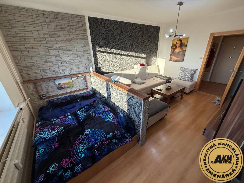 Living room with a sofa, bed, and wooden decor flooring in a three-room apartment.