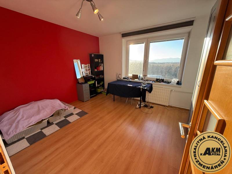 A room in a 3-room apartment with a red wall and a wooden decor floor.