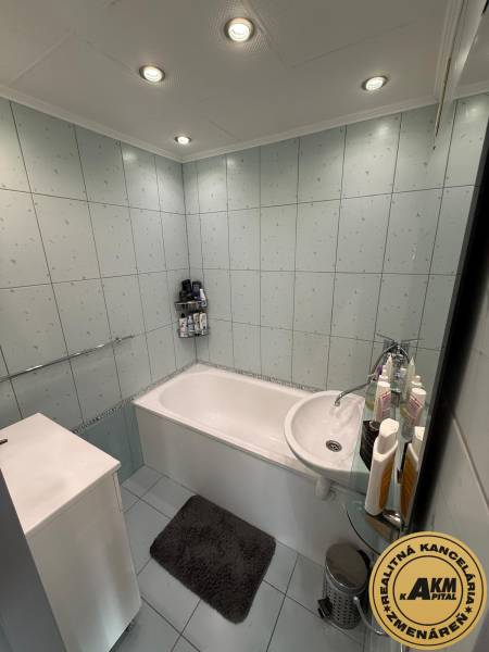 A bathroom with a bathtub, light tiles, and ceiling panel lighting in a 3-room apartment.