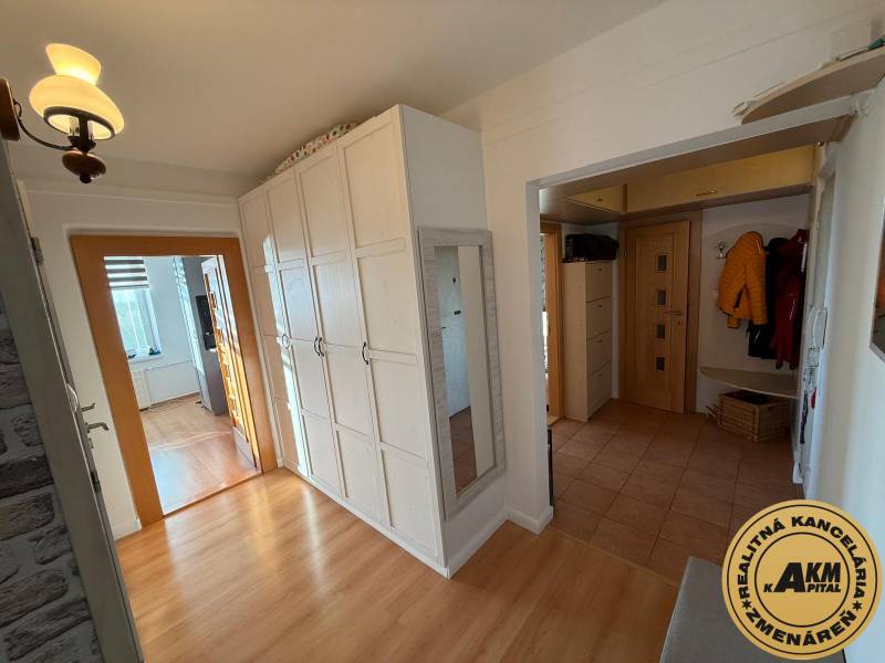 A hallway in a 3-room apartment with a wooden decor floor, white cabinets, and a mirror.