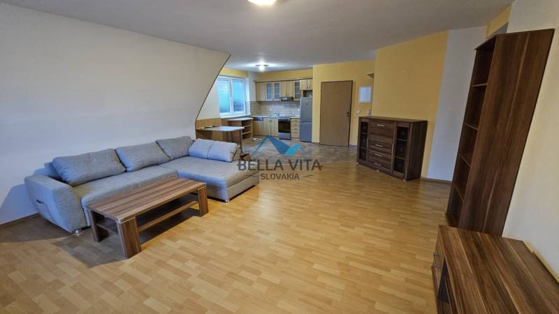 Interior with a sofa, kitchen, and wood-patterned flooring in a building.
