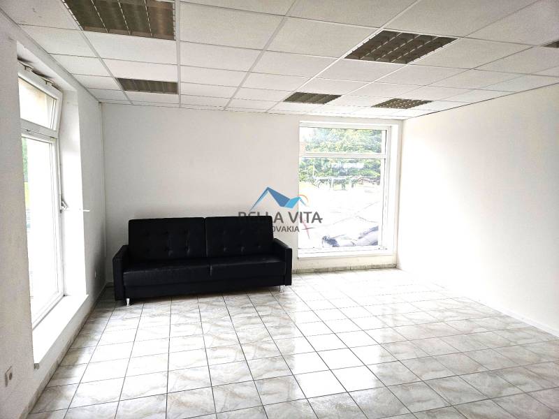 A room with a black sofa, light walls, tiles, and large windows in a building.