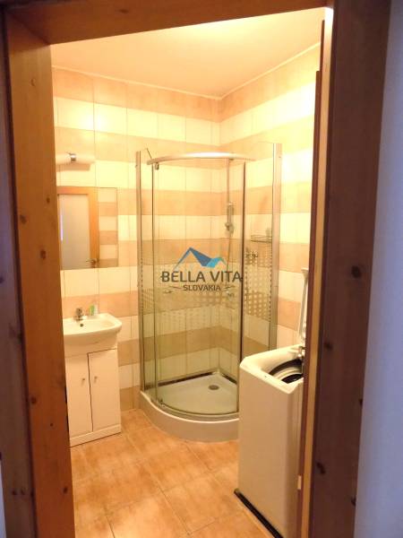 A bathroom in a building with tiles, a shower, and a washing machine.