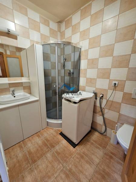 Bathroom with a washing machine, shower corner, tiled wall, and floor with a wooden decor.