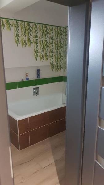 A bathroom in a family house with green leaf tiles and a bathtub.