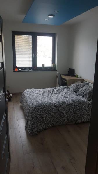 A bedroom in a family house with a bed, a desk, and a wooden decor floor.