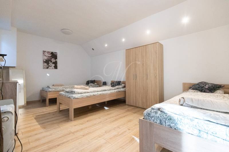 A bedroom in a one-room apartment with three single beds, a wooden decor floor, and a wardrobe.