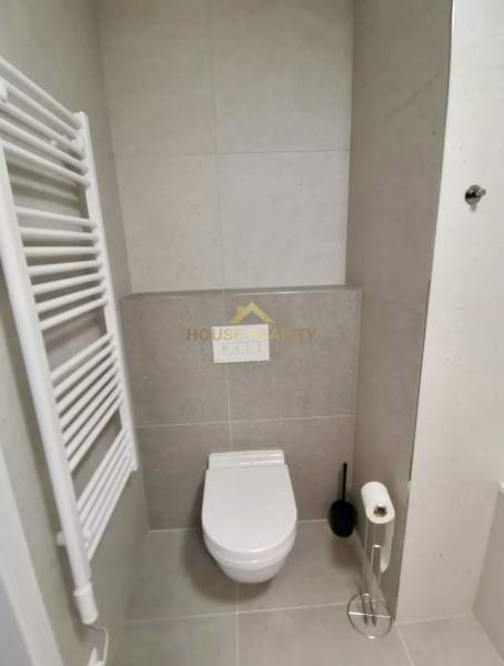 A bathroom with a toilet and a radiator in a studio apartment. Minimalist design with gray tiles.