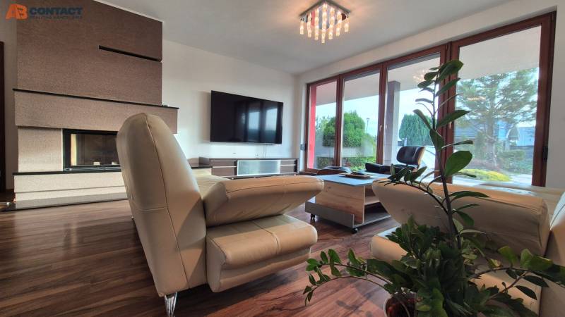 Living room of a family house with a leather sofa, fireplace, television, and wooden decor flooring.