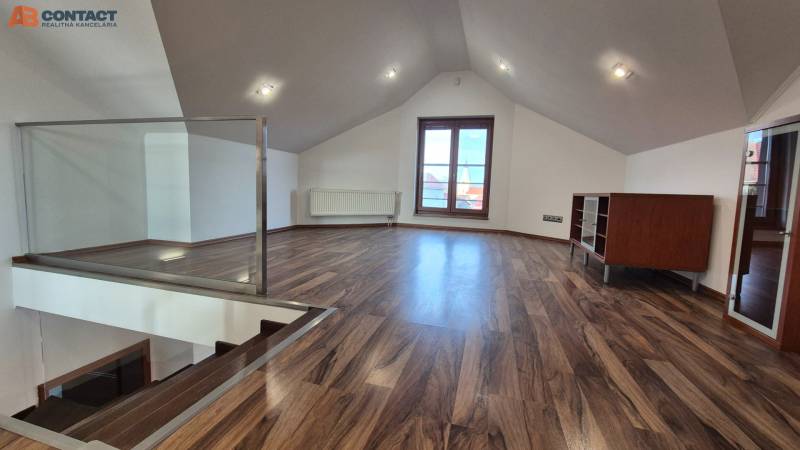 Attic room with wood-patterned flooring, staircase, and large window.