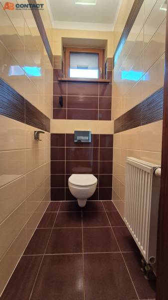 A toilet in a family house with brown and beige tiles and a window.