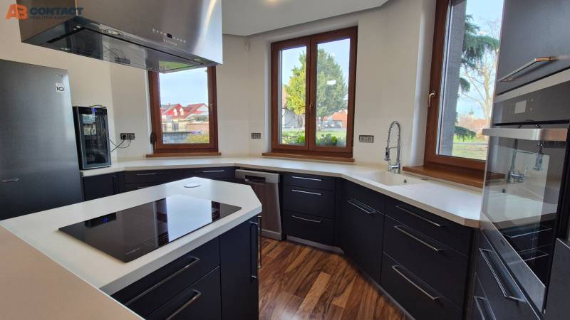A modernly furnished kitchen in a family house with white walls, black cabinets, and a wood-patterned floor.
