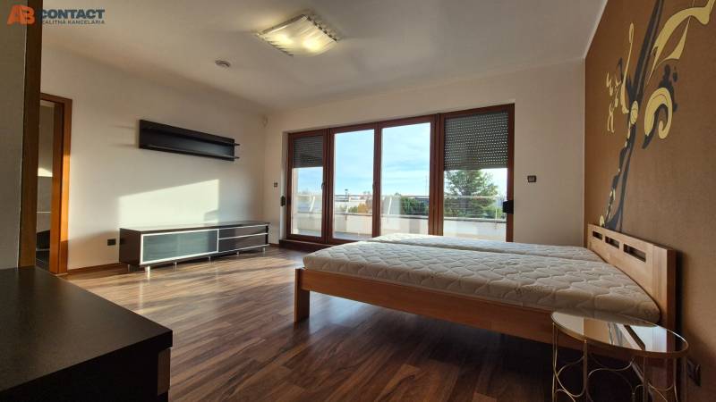 A bedroom in a family house with a wooden decor floor, a bed, and large balcony windows.