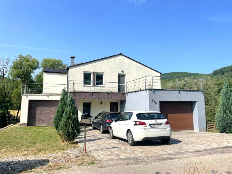 A family house in Melčice-Lieskové with a garage, two cars, and a garden on a sloping plot.