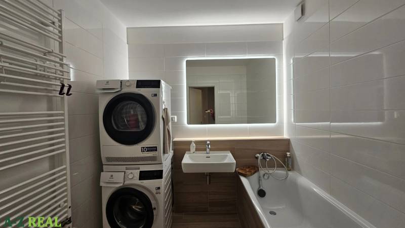 Bathroom with a bathtub, washing machine, dryer, and mirror in a 3-room apartment.