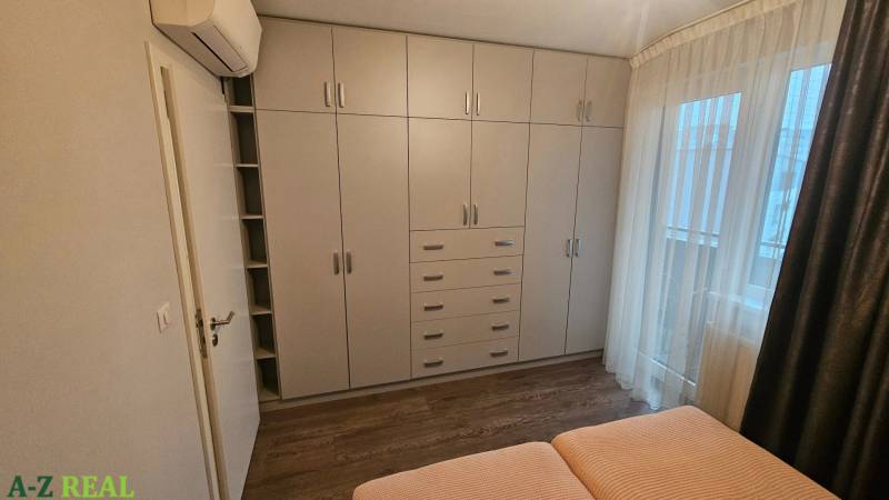 Bedroom with a white built-in wardrobe and a bed in a 3-room apartment with a wooden decor floor.