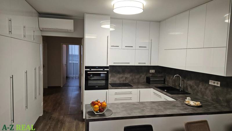 A kitchen with white cabinets, a dark countertop, and a wood-patterned floor in a 3-room apartment.