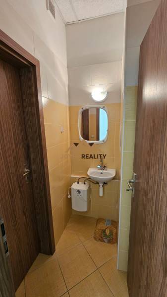 A bathroom in commercial premises with a sink and a mirror, tiled with light tiles.