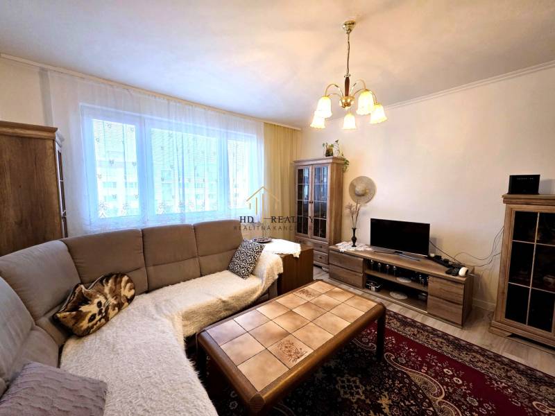 Living room of a three-room apartment with a sofa, chandelier, wood-patterned floor, and cabinets.