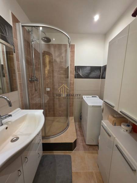 A bathroom in a 3-room apartment with a corner shower, sink, and washing machine.