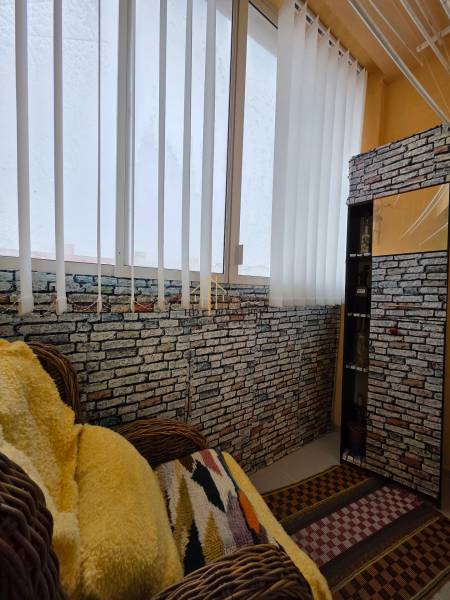 Interior of a 3-room apartment with a rattan chair, a wall with brick texture, and curtains.