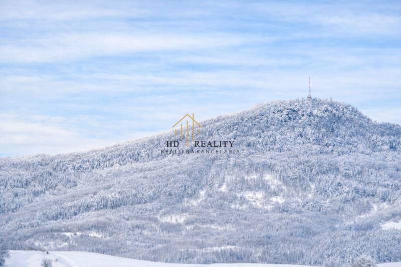 Snow-covered landscape with a dense forest and a transmitter on a hill near Banská Štiavnica.