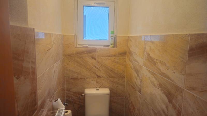 A toilet with ceramic tiles and a small window in a family house.