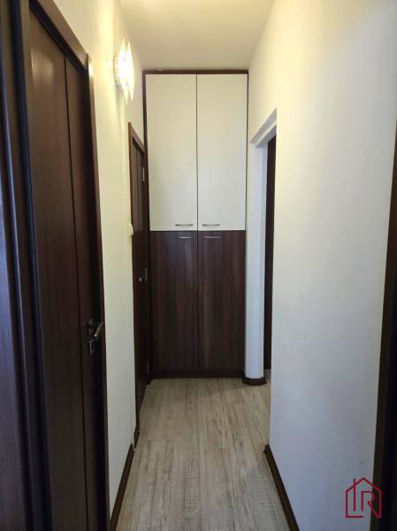 A narrow hallway in a 3-room apartment with a wooden decor floor and storage cabinets.
