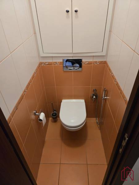 A toilet with tiles and a white cabinet in a 3-room apartment.