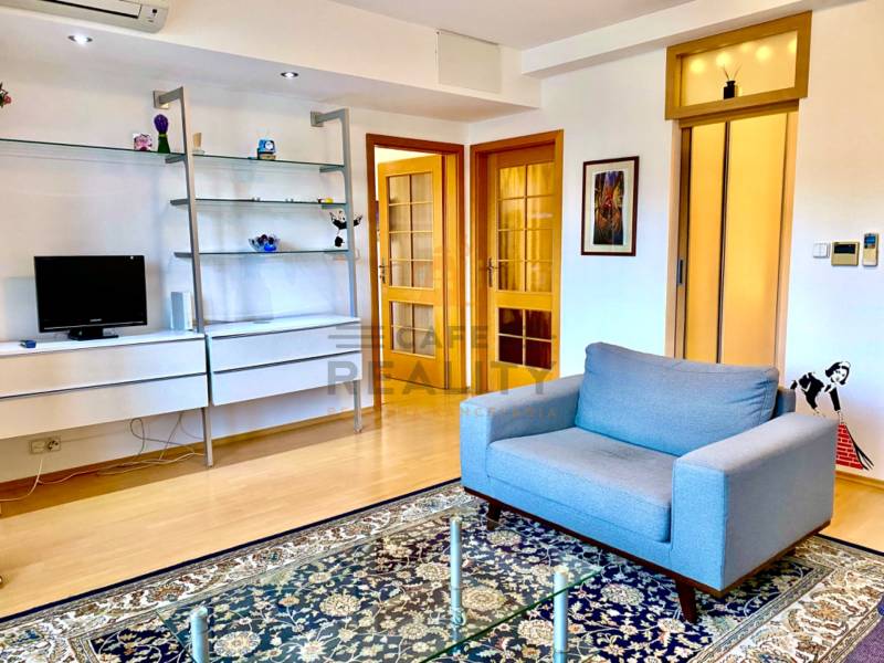 Living room with a sofa, shelves, carpet, and wooden decor flooring in a 2-room apartment.